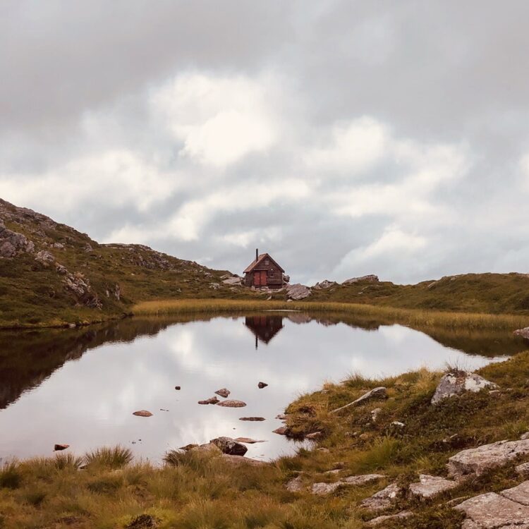 Cabin on green grass field near lake under white clouds 3689772