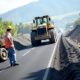 A group of construction workers operating an asphalt paver spreading fresh asphalt on a highway